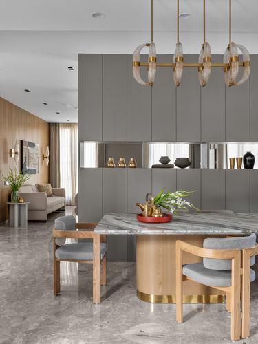 Dining table with marble top and brass base under a ringed pendant chandelier, grey cabinetry wall behind