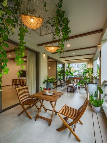 Long balcony with wooden folding furniture, rattan pendant lights, and trailing vines overhead.