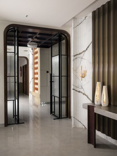 Marble-look feature wall with brass fluting beside a dark arched glass door in a foyer