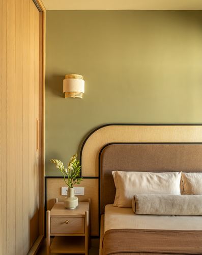 Bedroom corner with olive wall, arched cane-trimmed headboard, wood nightstand and cane sconce
