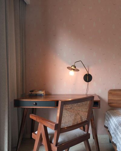 Wooden desk and cane-back chair against pink patterned wallpaper with a brass wall lamp