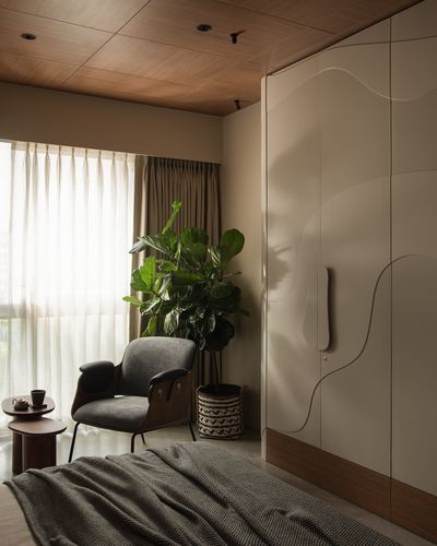 Bedroom corner with sculpted beige wardrobe, sheer curtains, fiddle leaf fig, and cane lounge chair