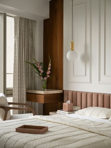 Bedroom corner with walnut wood column console, globe pendant, pink channel-tufted headboard, cane chair by curtained window
