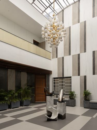 Double-height foyer with skylight, brass chandelier, striped marble wall and sculptures on plinths