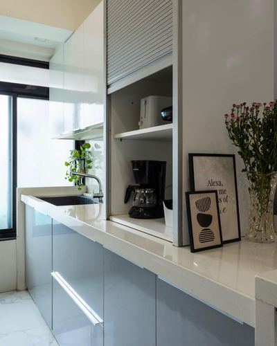 Galley kitchen counter with roller-shutter cabinet, coffee maker, framed prints and flowers