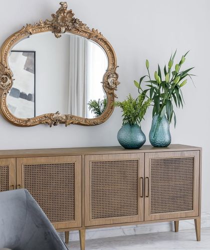 Gilded ornate mirror above a cane-front wood sideboard with teal glass vases