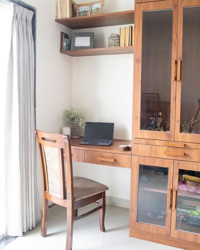 Wooden study desk with laptop and cane chair beside tall glass-front storage cabinet