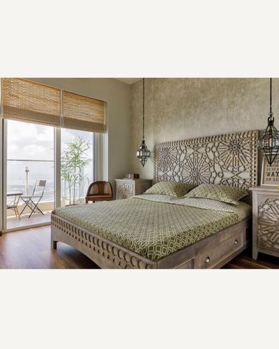 Bedroom with carved wood headboard, olive patterned bedding, and lantern pendants beside a balcony view