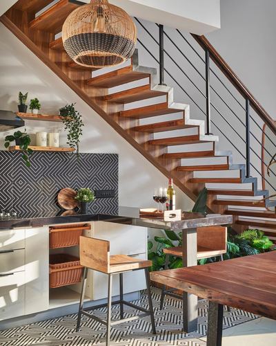 Kitchen and dining area under a wooden staircase with patterned tile backsplash and rattan pendant light
