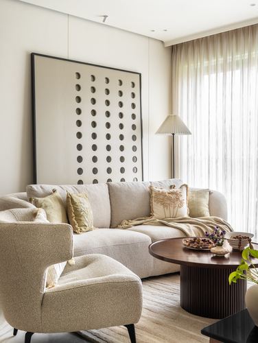 Beige living room with boucle sofa and armchair, fluted wood coffee table, and large dotted artwork.