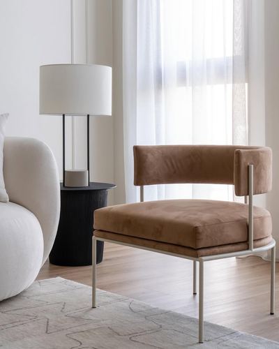 Tan velvet accent chair beside black fluted side table and cream curved sofa near sheer curtains
