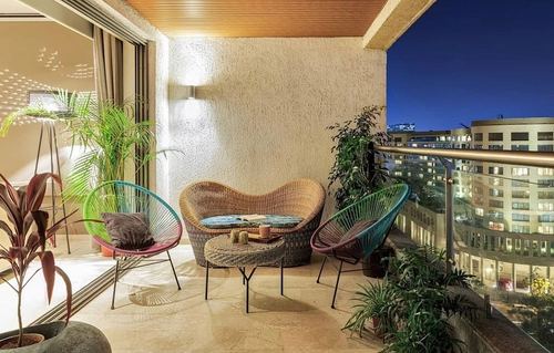 Balcony seating with woven loveseat and acapulco chairs overlooking city skyline at dusk