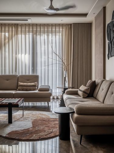 Beige living room with sectional sofa, round rug, sheer curtains and marble floor