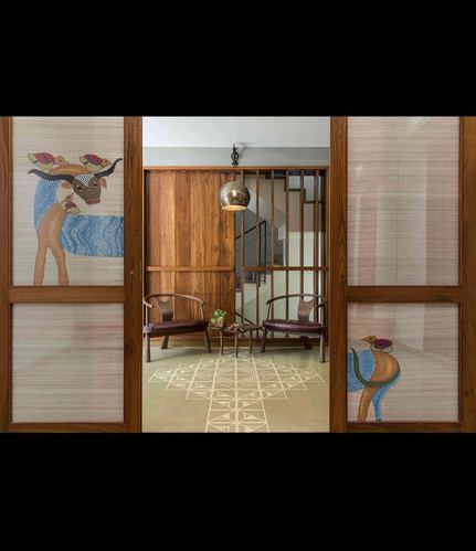 Foyer viewed through Gond-art sliding doors, wooden chairs and patterned floor beyond