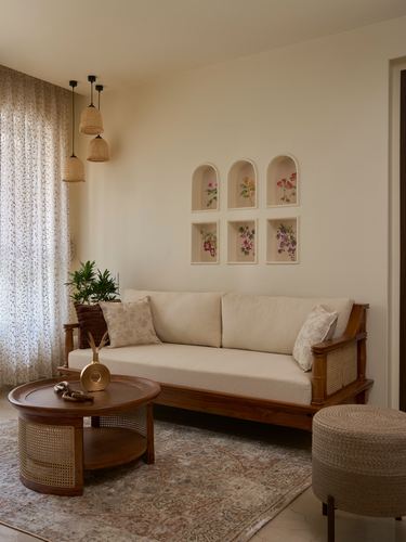 Cream sofa with cane frame beneath arched wall niches holding floral art, cane coffee table in front
