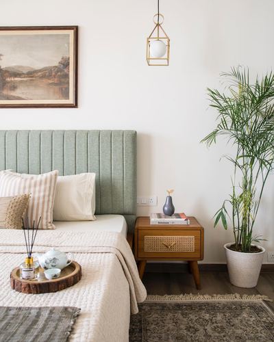 Bedroom corner with green tufted headboard, cane nightstand, pendant light and potted palm