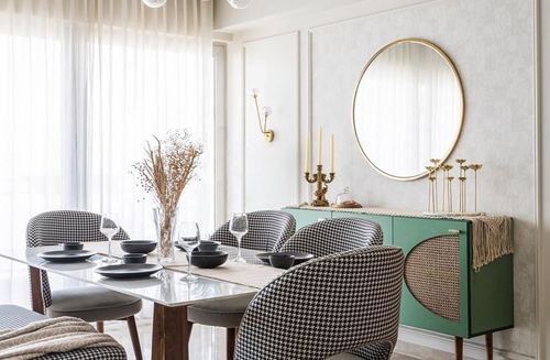 Dining table with houndstooth chairs facing a green sideboard and round brass mirror