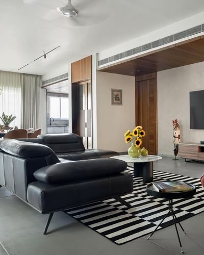 Living room with black leather sofa, marble coffee table, sunflowers, and striped rug