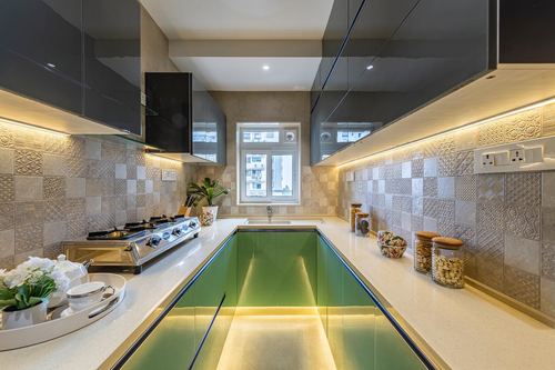 U-shaped modern kitchen with green cabinetry, glossy black overheads, and textured beige tile backsplash