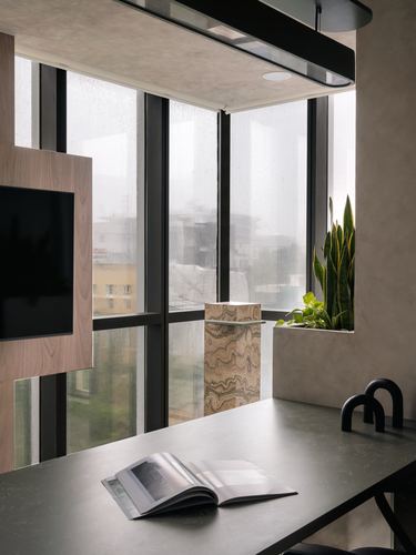 Corner workstation with dark desk, rain-streaked windows, and a marbled stone pedestal by a planter