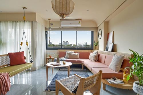 Living room with pink sectional, cane swing, round coffee table and city view through windows