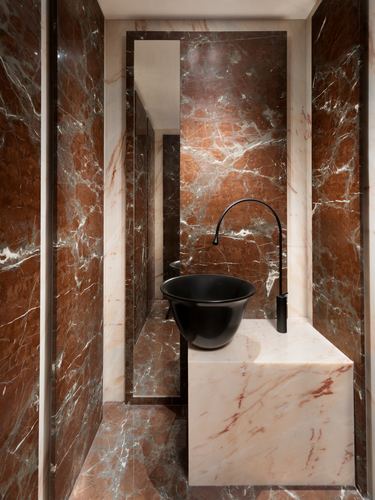 Powder room with dark veined marble walls and a black vessel sink on a marble block