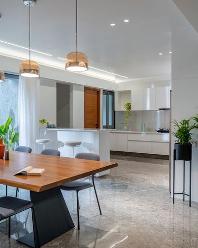Open kitchen and dining area with wooden table, marble floor, amber pendant lights and white cabinetry