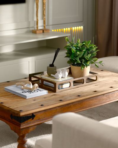 Styled wooden coffee table with tray, plant, diffuser and books in front of beige built-in shelving