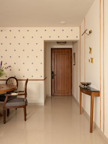 Foyer with wooden door, patterned wallpaper, and slim console table under brass sconce