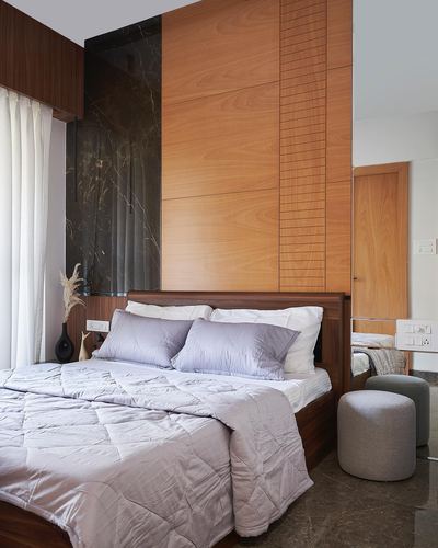 Bedroom with wood-panelled wall, dark stone accent, and grey bedding with round ottomans