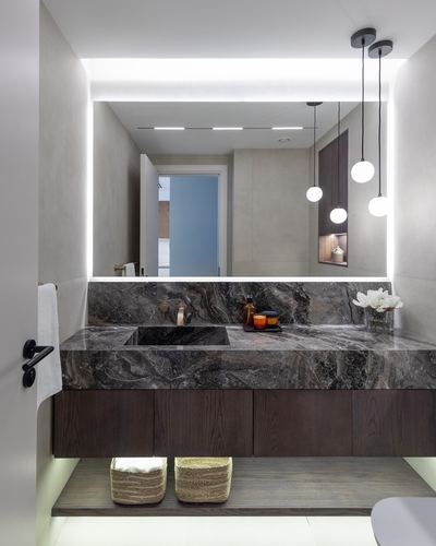 Bathroom with backlit mirror, dark stone vanity, floating wood cabinetry, and hanging globe pendants