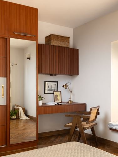 Wooden wardrobe with mirror beside a floating desk and cane chair in a bedroom corner