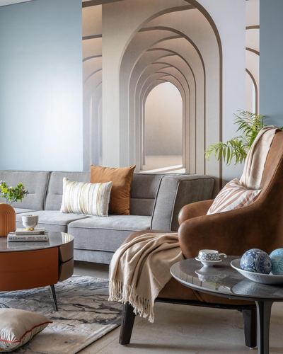Living room corner with grey sofa, tan leather chair, and arched mural wallpaper behind