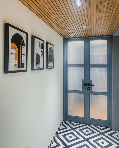 Foyer with slatted wood ceiling, framed prints on white wall, and fluted glass double doors above patterned tile floor