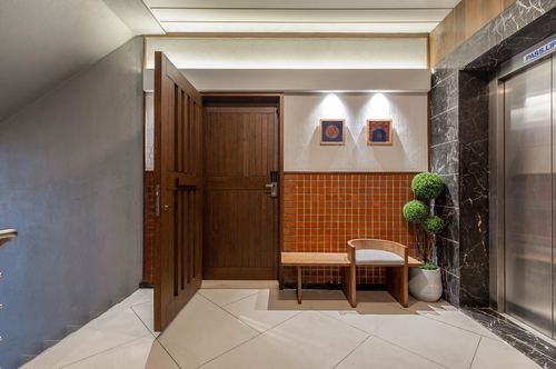 Entry foyer with wooden door, terracotta tile wall, bench, and marble-clad elevator wall
