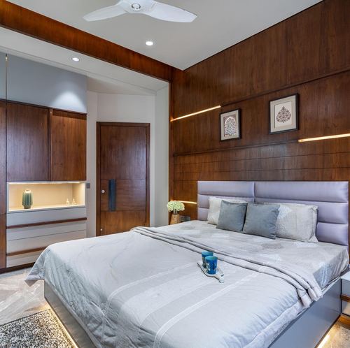 Bedroom with wood-panelled wall, channel-tufted grey headboard, and backlit display niche