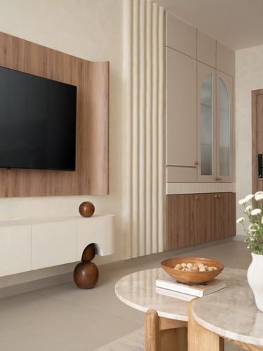 Beige living room with wood-panel TV wall, fluted plaster column, and arched-glass storage cabinet