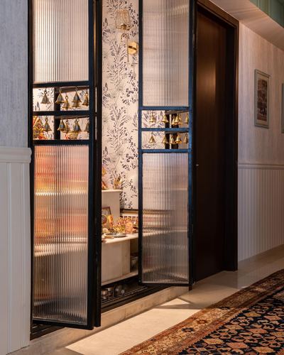 Pooja unit with fluted glass doors, hanging bells, and floral wallpaper backdrop in a hallway