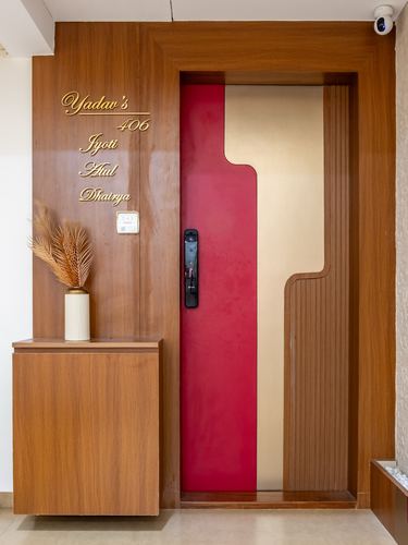 Wooden entrance door with magenta lacquered panel, brass nameplate, and console with dried leaves in vase.