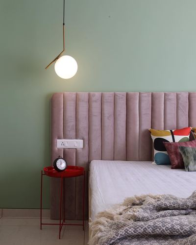 Sage green bedroom wall with pink channel-tufted headboard and sculptural pendant light