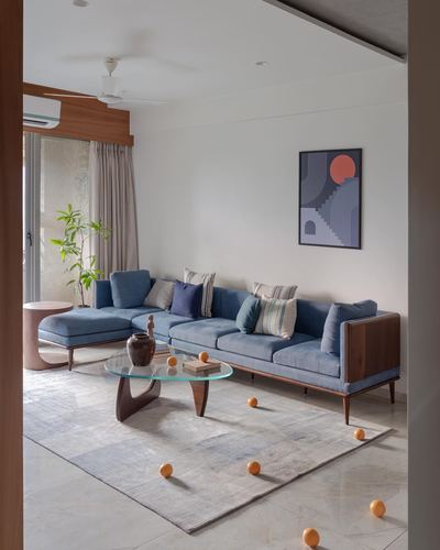 Living room with blue sectional sofa, wood-legged glass coffee table, and abstract wall art