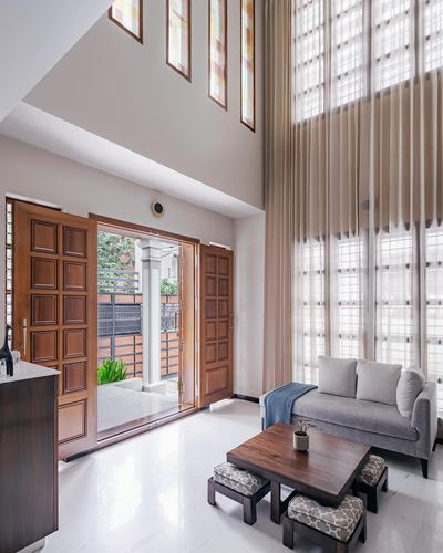 Double-height foyer with carved wooden door, sheer curtains, and grey sofa on marble floor