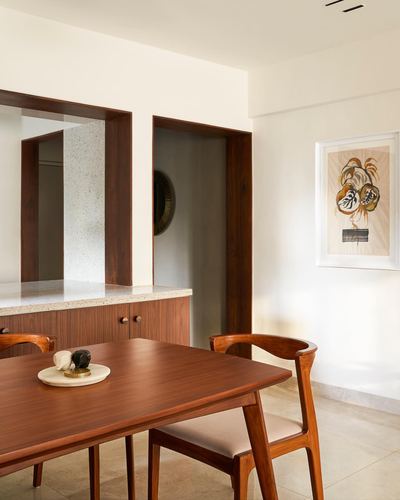 Wooden dining table with curved chairs beside terrazzo counter and wood-framed niches