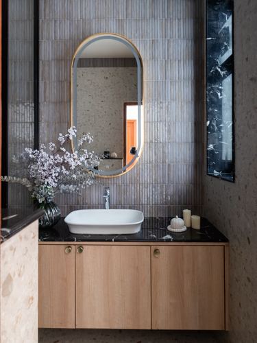 Bathroom vanity with oval mirror, wooden cabinetry, dark stone counter and white vessel sink