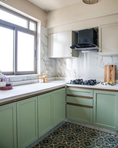 L-shaped sage green kitchen with marble backsplash, black chimney hood, and patterned floor tiles