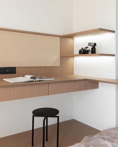 Wooden desk with cameras on lit corner shelf and black stool below