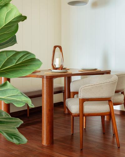 Wooden dining table with houndstooth chairs, bench, and fiddle leaf fig against paneled cream wall