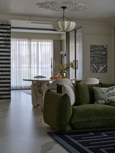 Living room with green velvet sofa, marble dining table, and decorative pendant light