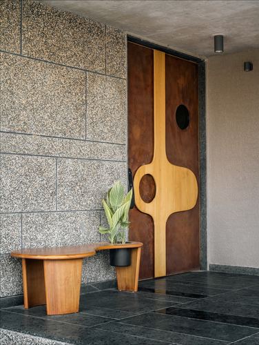 Entrance door with sculptural wood inlay and circular cutouts beside a wooden bench and plant