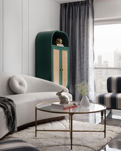 Curved white sofa beside arched green cane cabinet and round brass coffee table